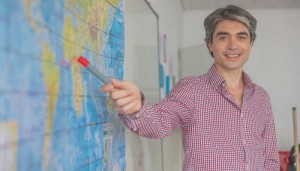 Male teacher in the classroom teaching geography pointing to a world map