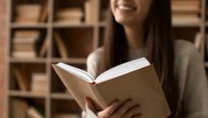 Beautiful young woman reading book in library, closeup