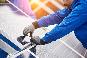 Smiling male technician in blue suit installing photovoltaic blue solar modules with screw. Man electrician panel sun sustainable resources renewable energy source alternative innovation