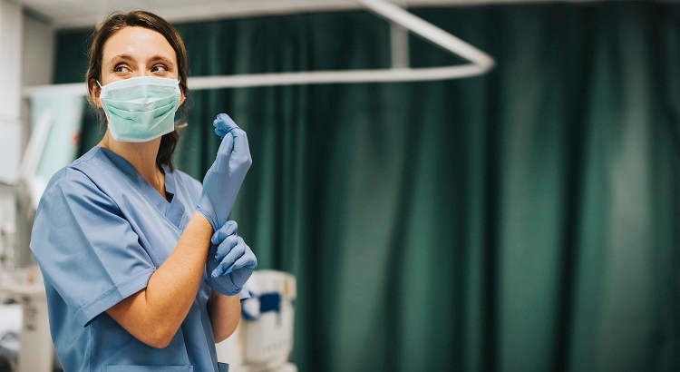 Enfermera con una mascarilla poniéndose guantes. | rawpixel