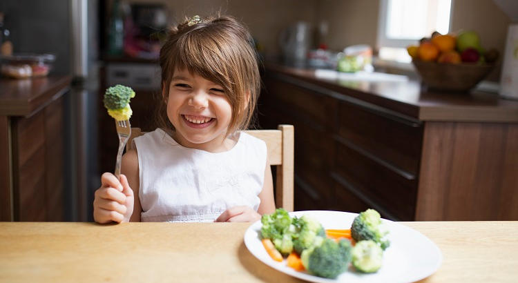 Niña comiendo verdura en la cocina. | freepik