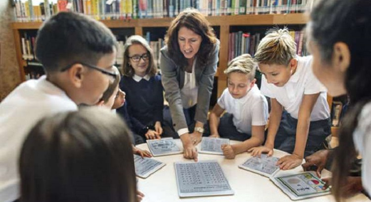 Profesora con alumnos en el aula utilizando dispositivos tecnológicos. 