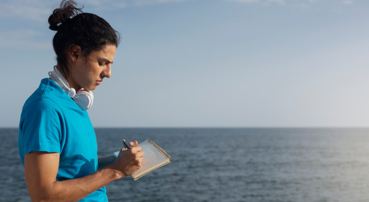 Joven en la playa apuntando opciones sobre qué estudiar a partir de septiembre, | Foto: Magnific