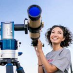 girl looking through a telescope outdoors